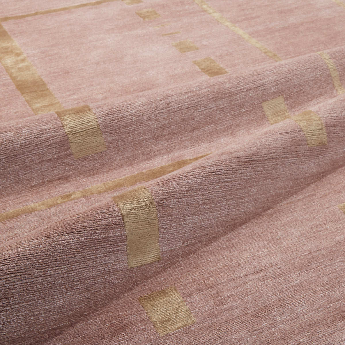 A close-up of a textured fabric in a dusty rose pink color with woven gold geometric stripe and square patterns.