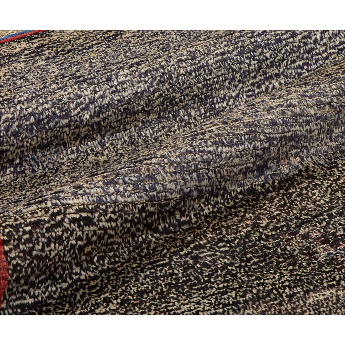 A close-up of a textured woven fabric with a mottled pattern of black, beige, and gray threads, draped to show its texture and weave.