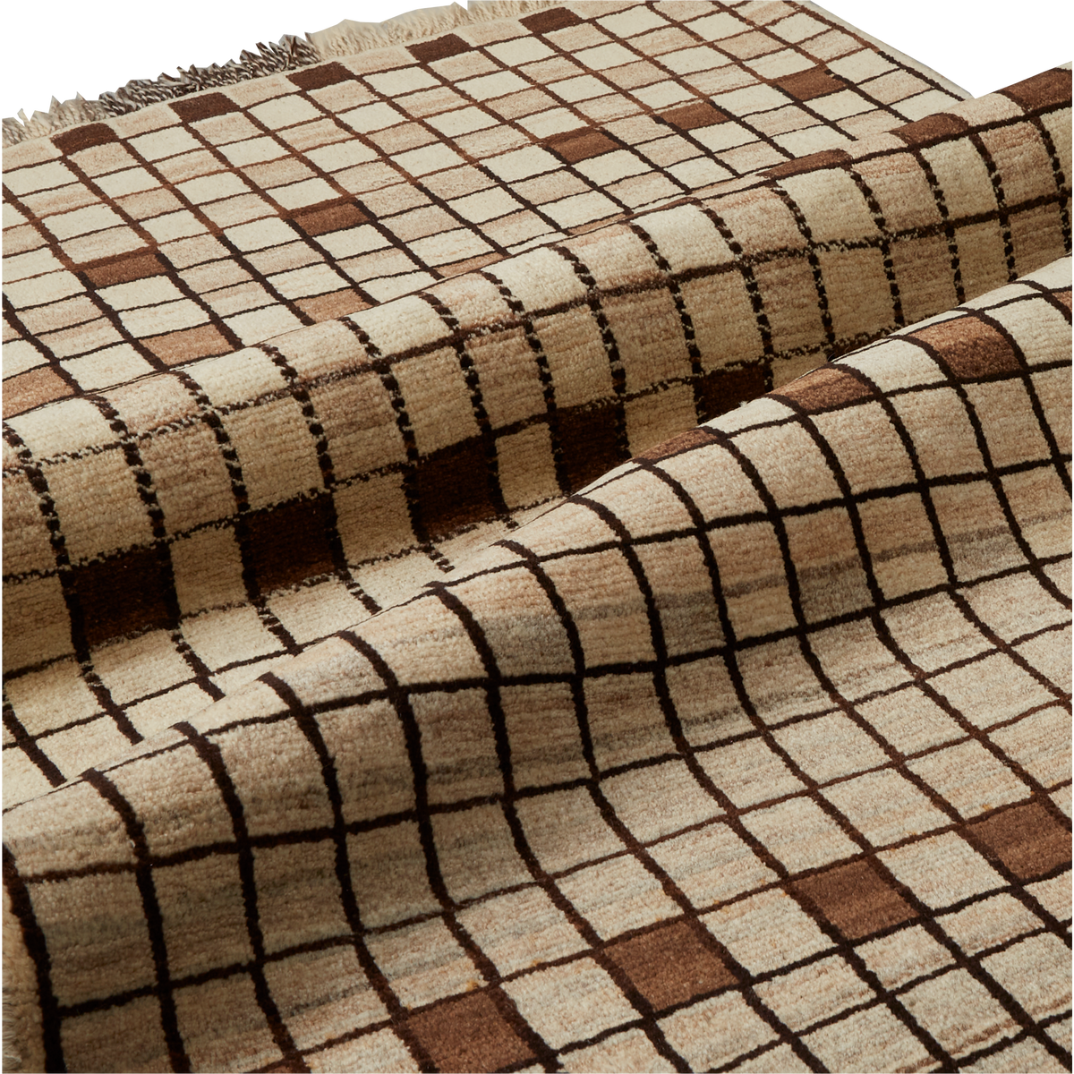 A close-up of a woven area rug with a beige and cream base, featuring a dark brown grid pattern and matching brown square accents. The rug is draped to show its texture and pattern, with a fringed edge visible at the top.