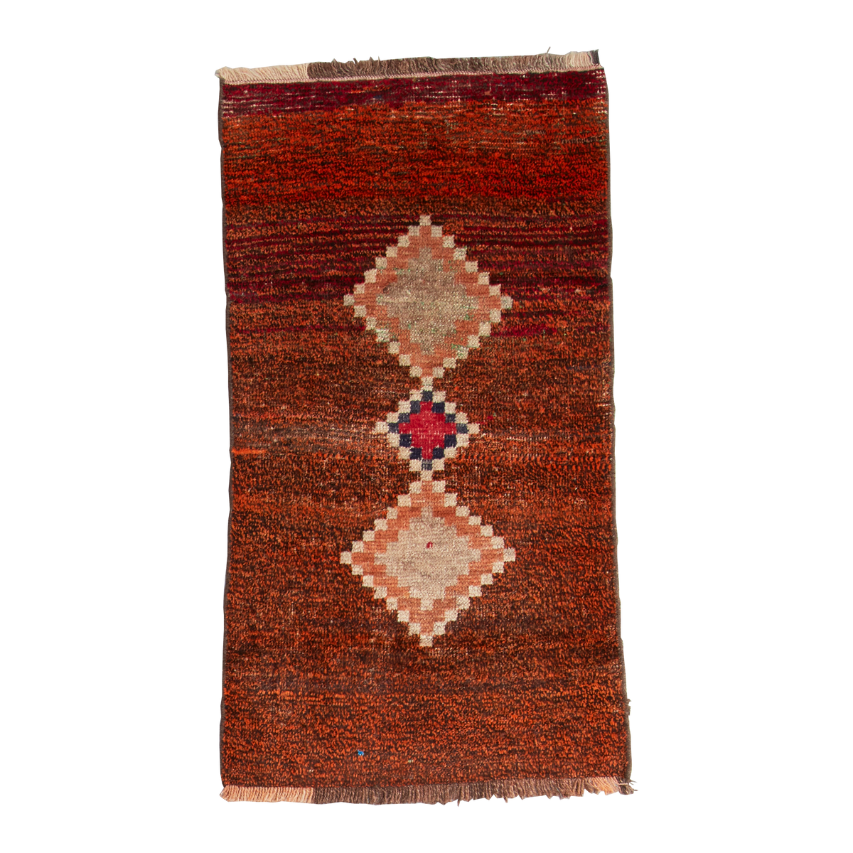 A rectangular handwoven kilim rug with a textured rust-brown base, featuring two large diamond motifs and a central smaller diamond in beige, pink, and red, finished with fringed edges.