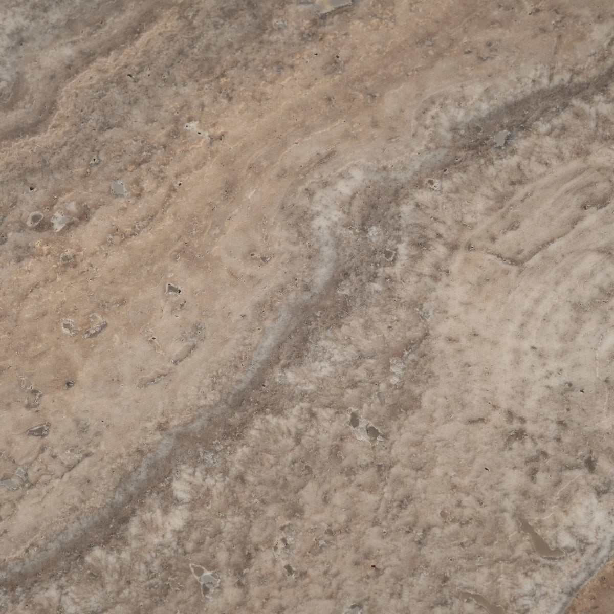 Close-up showing the Taupe travertine surface of the Duvall Side Table, with cream and ivory mottling, small natural voids, and warm tan streaks across a grey-taupe ground.