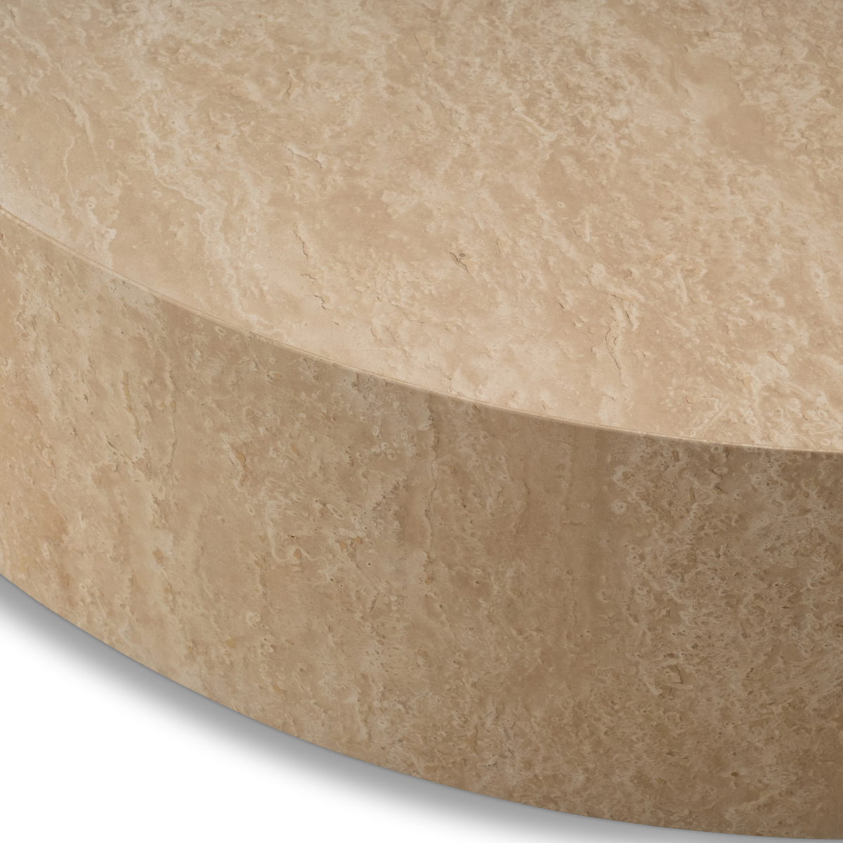 Close-up showing the edge of the Meta Round Coffee Table in Warm Beige travertine, with the crisp rim where the honed top meets the curved side and small natural pits in the stone.