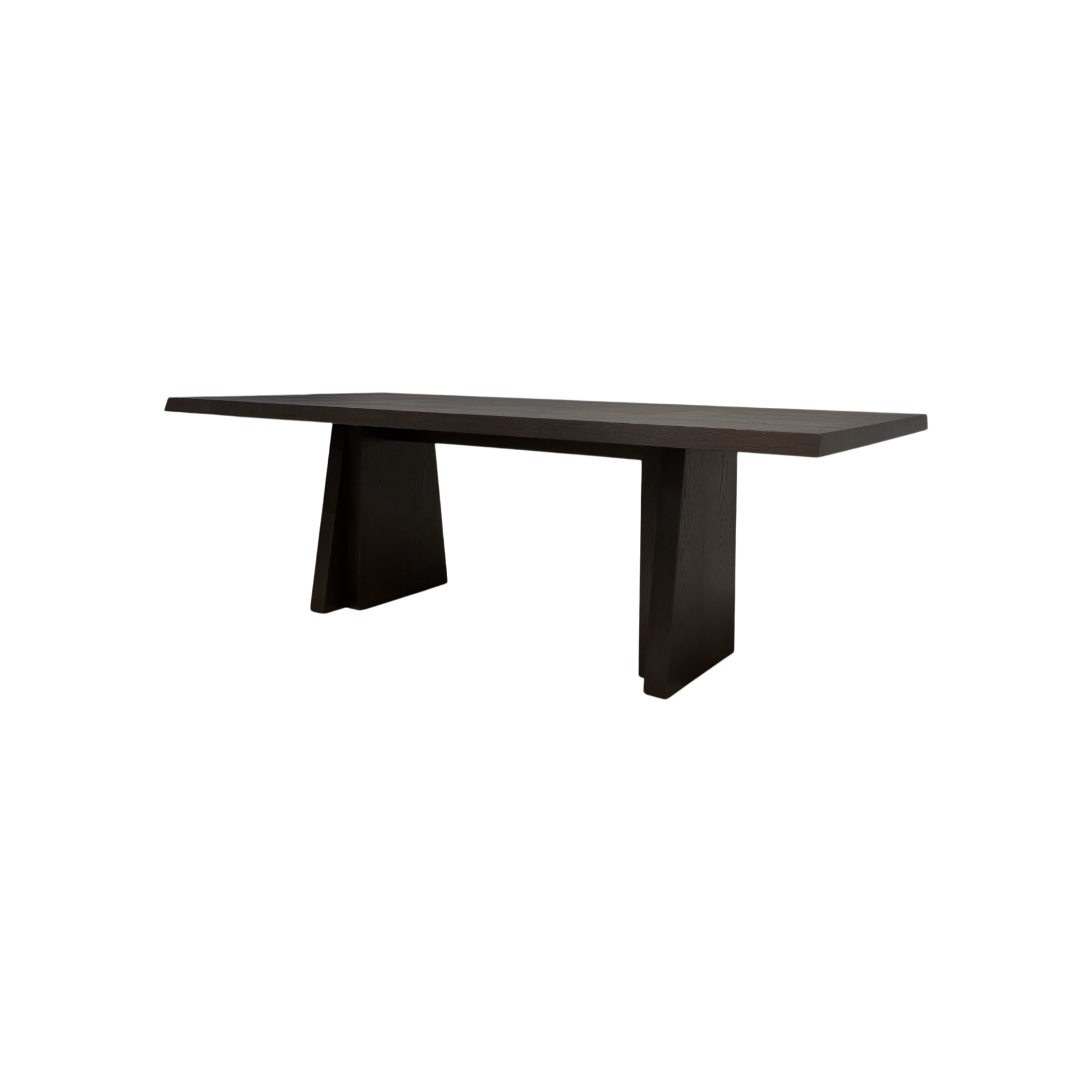 Angled view of the Oblique 96-inch Dining Table showing its elongated dark wood top, chamfered edges and sculptural splayed pedestal bases.