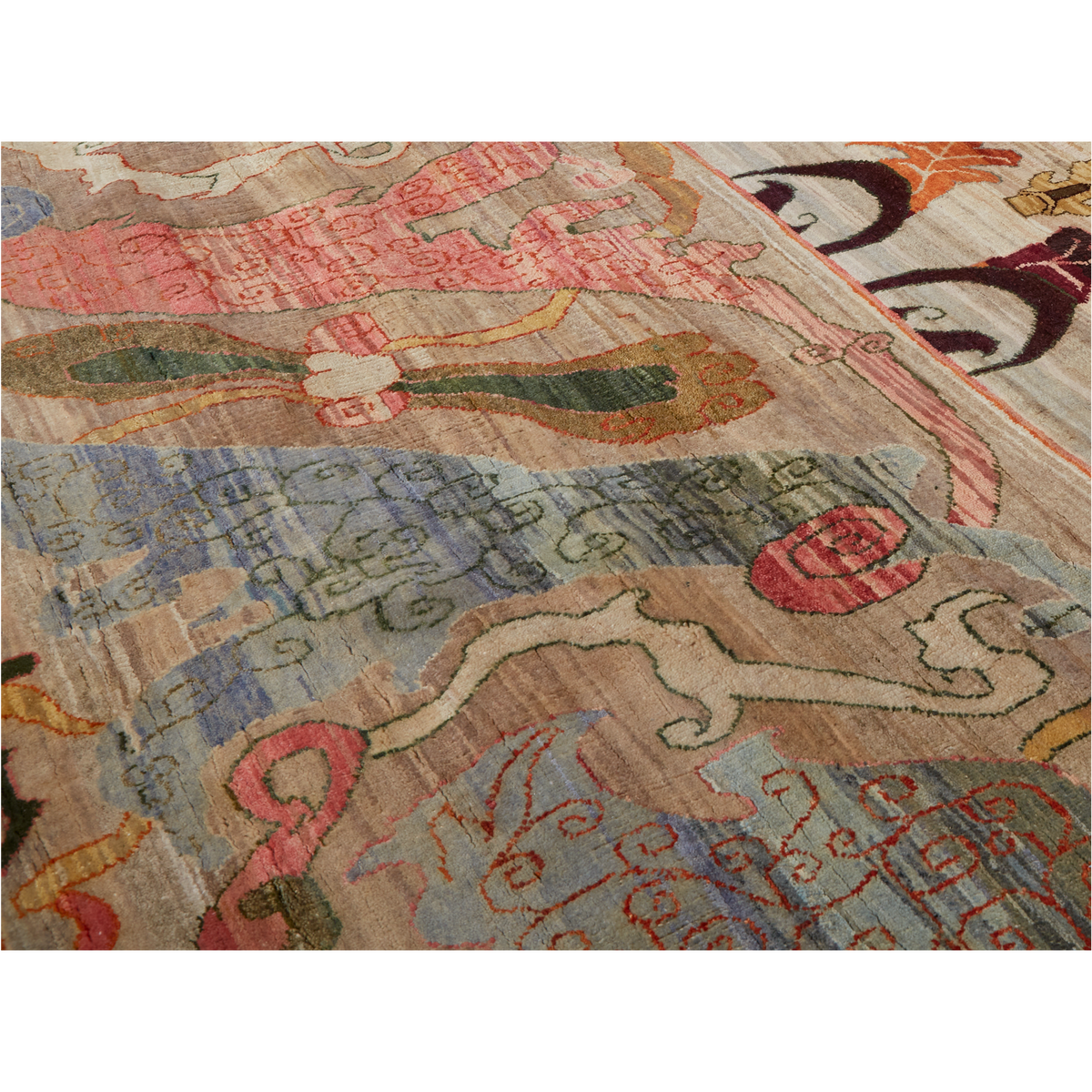 A close-up of a patterned area rug with an abstract, folk-inspired design featuring pink, blue, green, and orange motifs on a beige background.