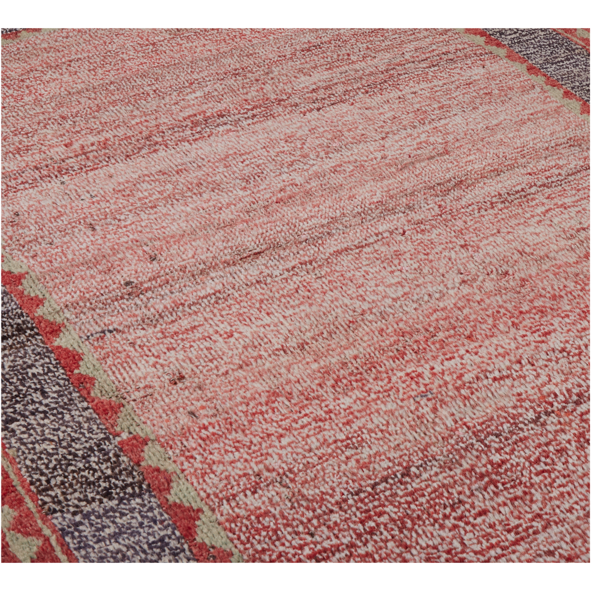 A close-up of a textured area rug with a distressed, hand-woven appearance. The dominant color is a muted dusty rose or terracotta red, mixed with cream and gray in a heathered pattern, with a geometric border visible on the bottom left.