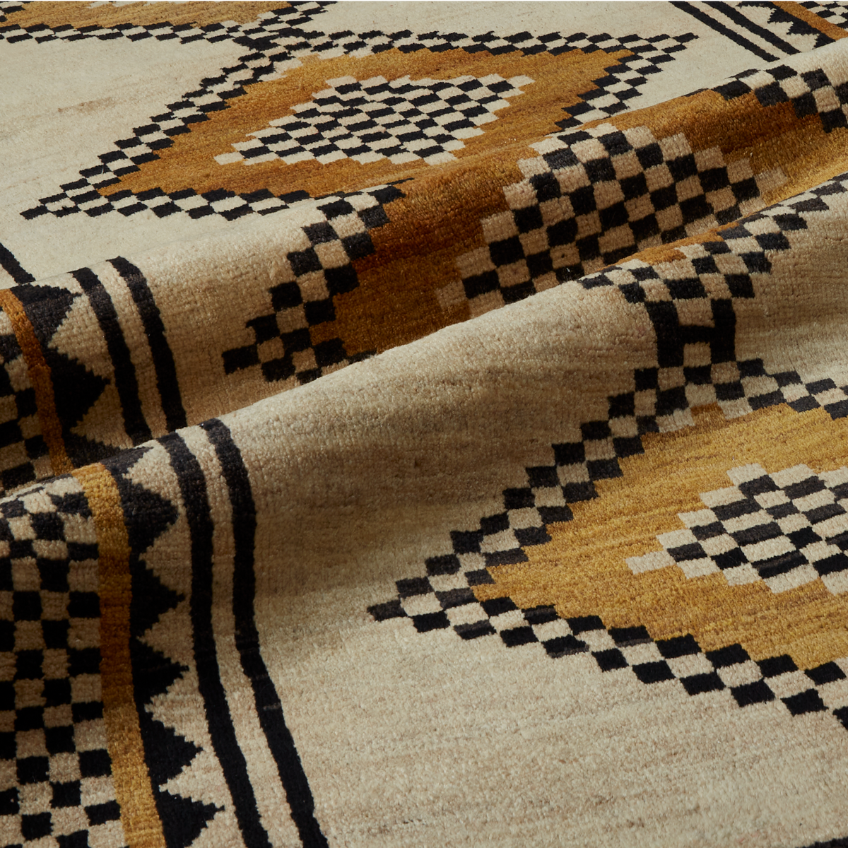 A close-up of a woven textile with a Southwestern geometric pattern in beige, black, and ochre brown, showing the texture and folds of the fabric.