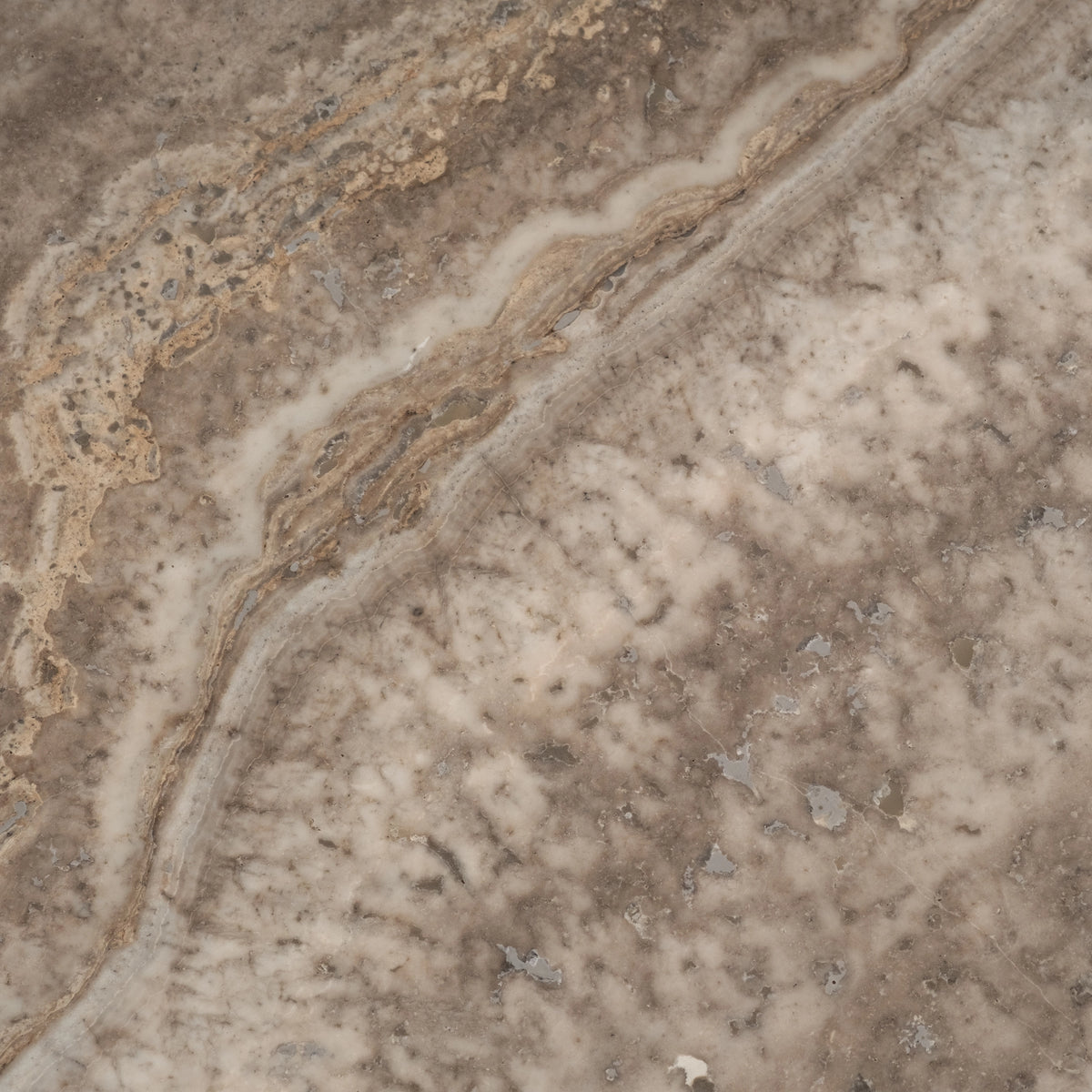 Close-up showing the Taupe travertine surface of the Duvall Coffee Table, with a wavy cream and tan vein running diagonally across a grey-taupe ground, small natural voids, and soft ivory mottling.