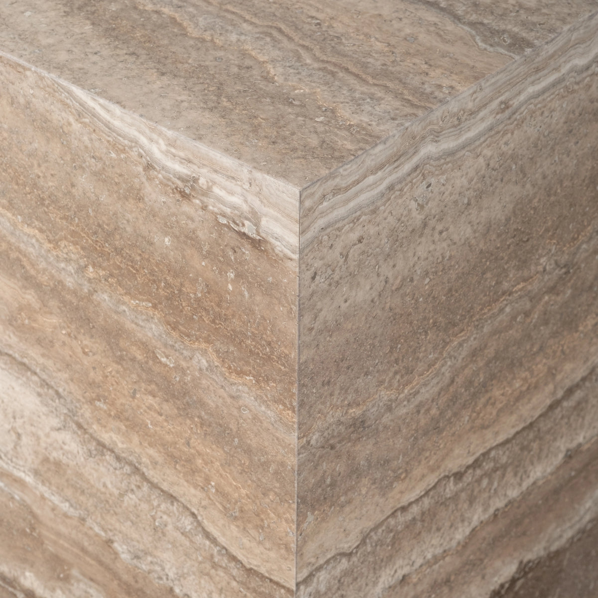 Close-up of the corner of the Duvall Side Table in Taupe travertine, showing the crisp edge where the honed top meets the layered, wavy-banded sides.