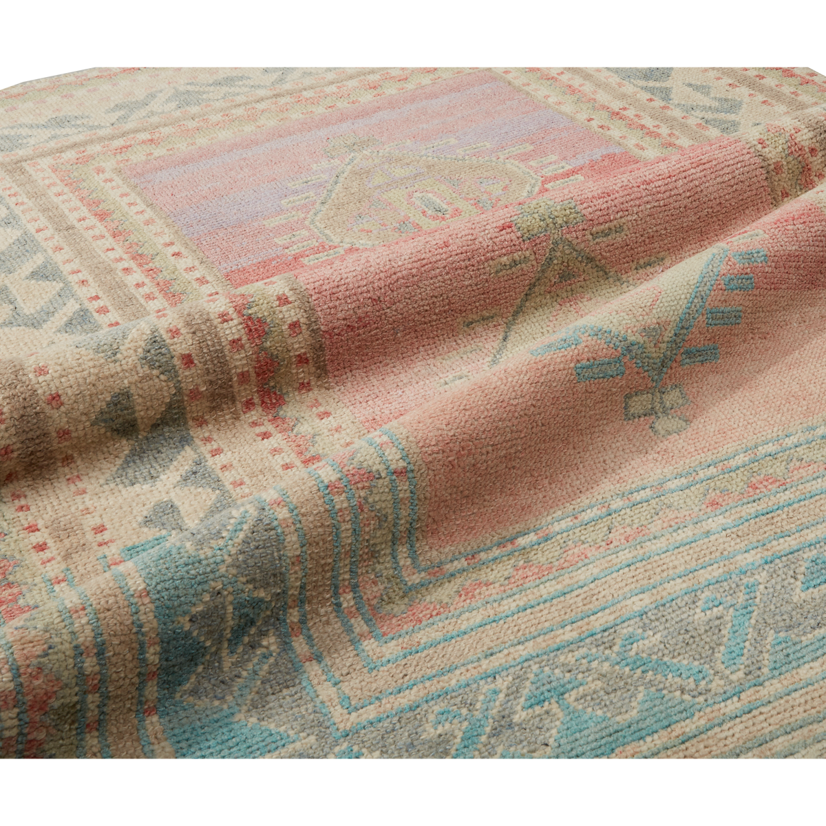 A close-up of a woven textile or rug with a soft pink center, beige border, and blue and red geometric patterns.