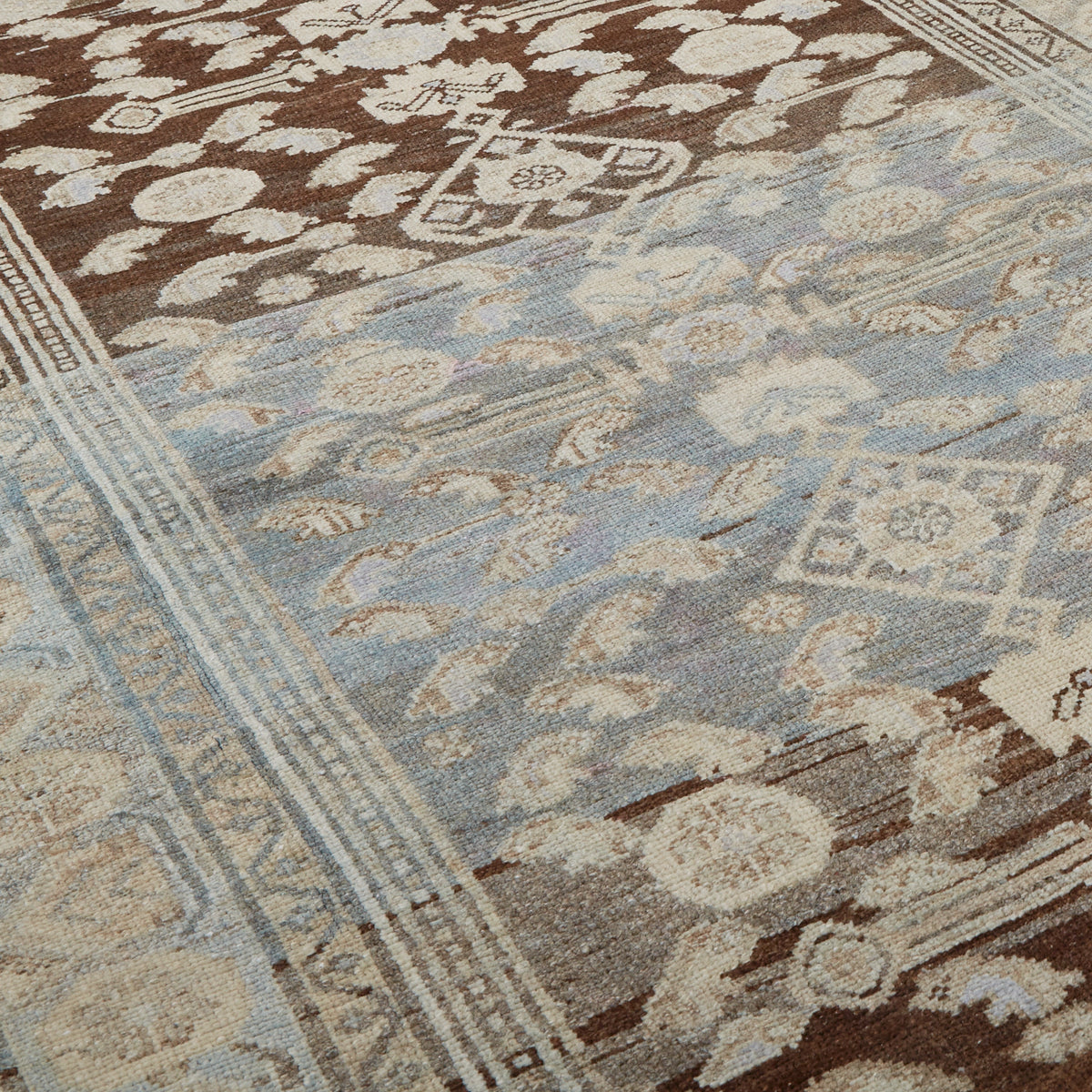 A close-up of a traditional patterned rug with a light blue field, brown borders, and cream floral motifs.