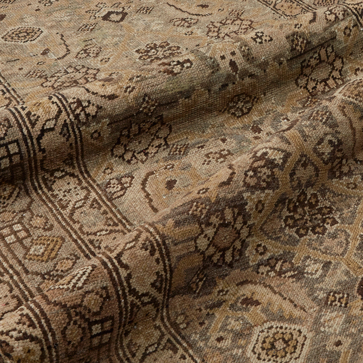 A close-up of a woven textile with an intricate traditional pattern in beige, brown, and tan tones, showing the fabric's texture and folds.