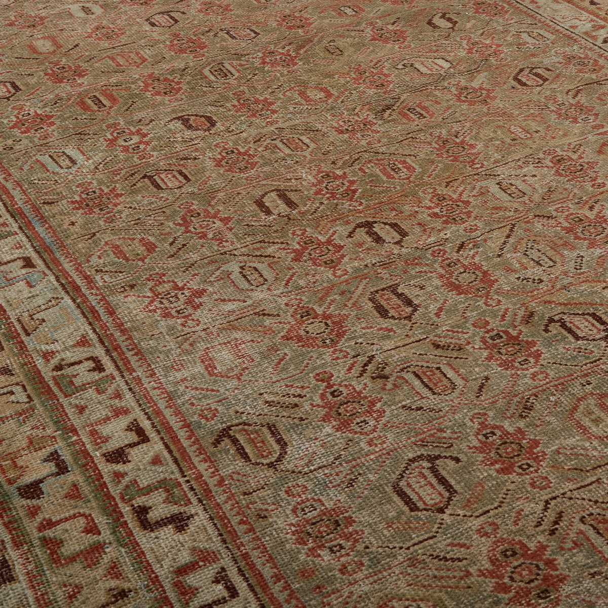 A close-up view of a traditional patterned rug with a beige base, featuring red and brown floral motifs and a decorative border.