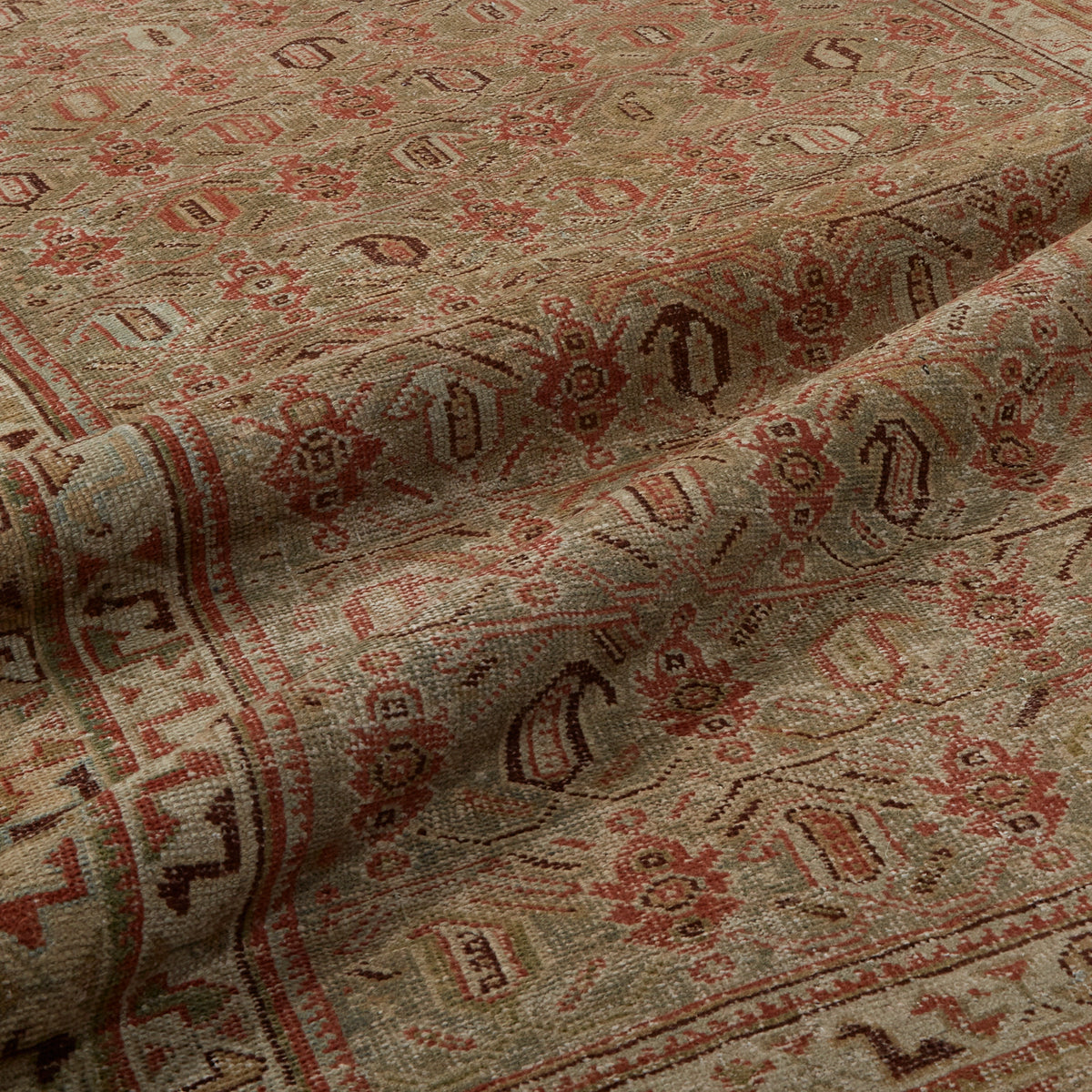 A close-up of a folded area rug with a traditional Persian-style pattern in beige, rust red, and brown.