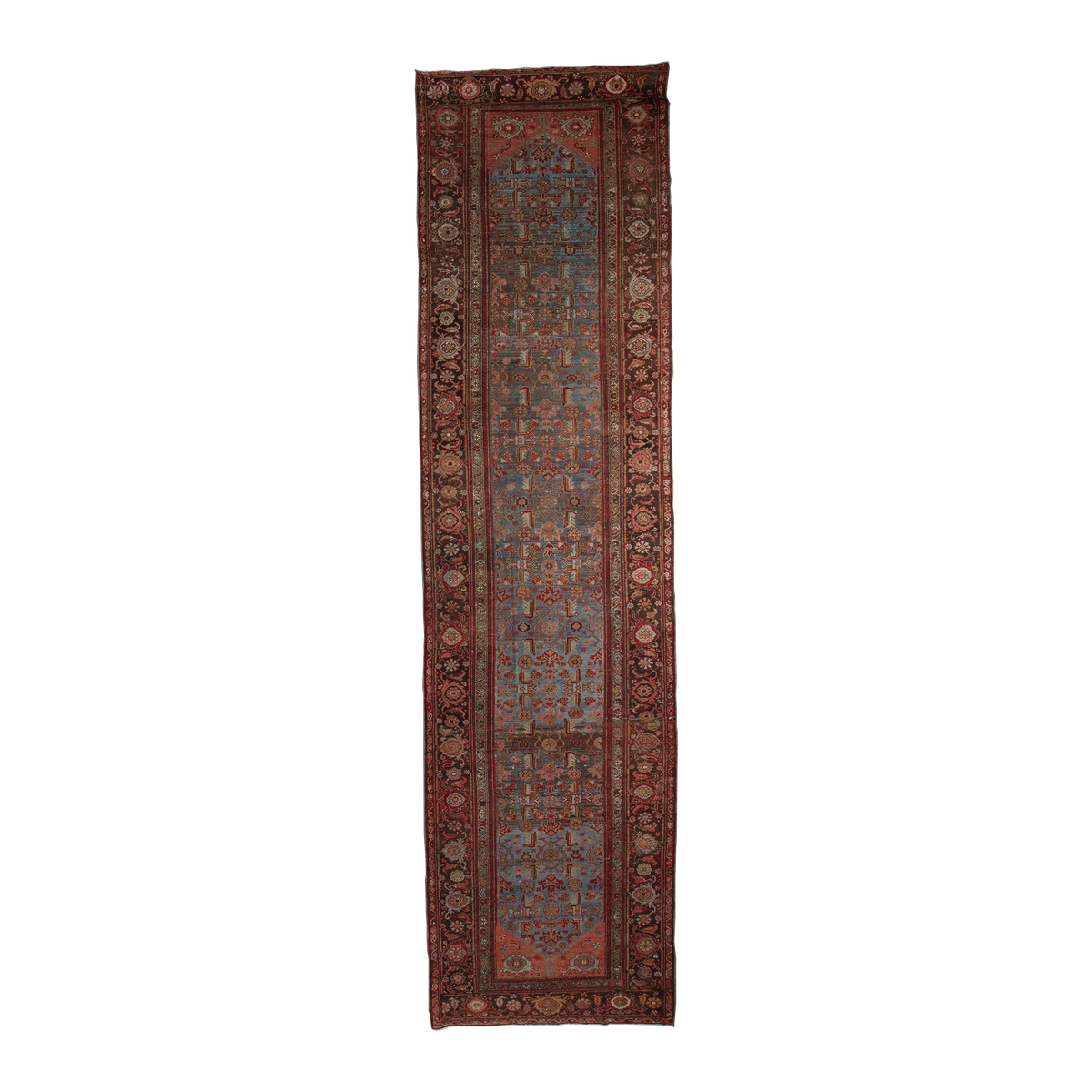 A long, narrow traditional runner rug with an intricate geometric and floral pattern in rust red, blue, beige, and brown tones, shown flat against a solid white background.