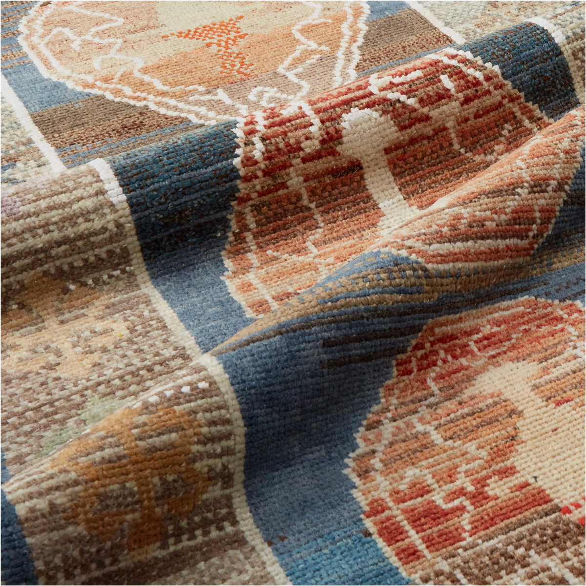 A close-up of a woven rug with a geometric and tribal-inspired pattern in shades of blue, terracotta, beige, and brown.
